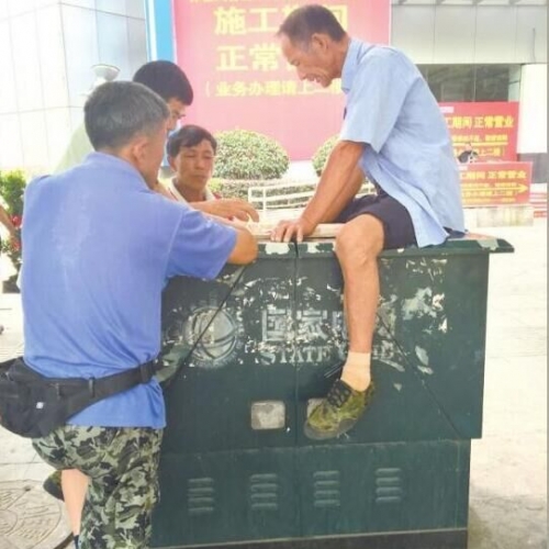 浔城几名男子坐在电箱上与人下棋